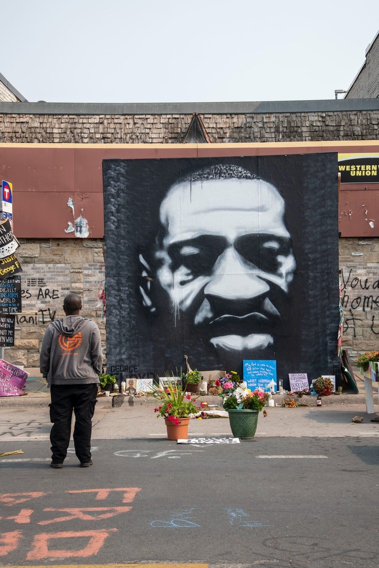 man standing in front of George Floyd memorial, black and white graffiti 