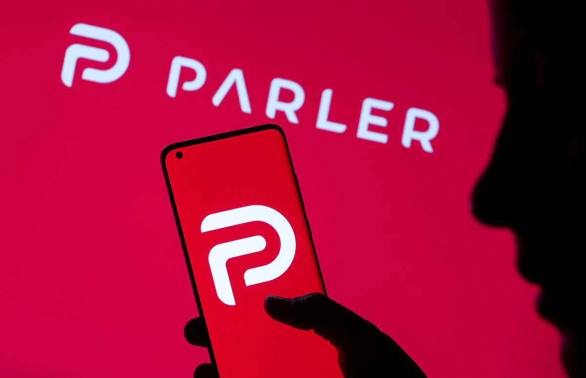 image of parler logo on a red background. in the foreground is a silhouette holding a mobile phone with the Parler logo on it NFT.
